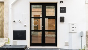 Entrada moderna de un edificio con puerta de vidrio de marco negro, un pequeño espacio de asientos al aire libre y un letrero que indica "Suite Maior".
