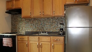 Uma cozinha com armários de madeira, geladeira de aço inoxidável, fogão e painel de azulejos.
