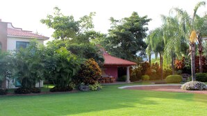 Um jardim bem cuidado com um pavilhão de telhado vermelho, vegetação exuberante e gramado aparado.