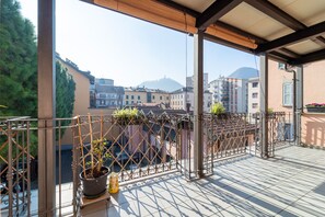 A balcony with a view of buildings and mountains, featuring a metal railing and potted plants. - Gerbett Apartment with Terrace by Wonderful Italy (Como)