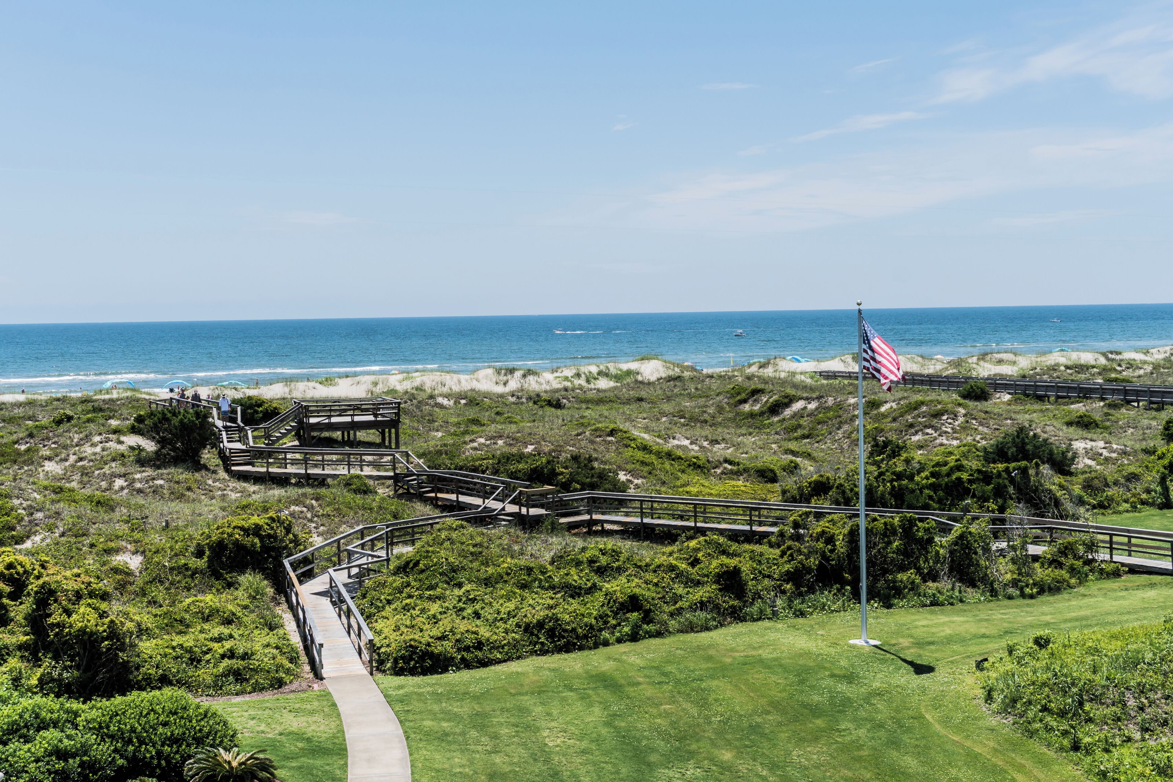 A coastal golf course with a wooden bridge, a flagpole with an American flag, and a clear view of the ocean.