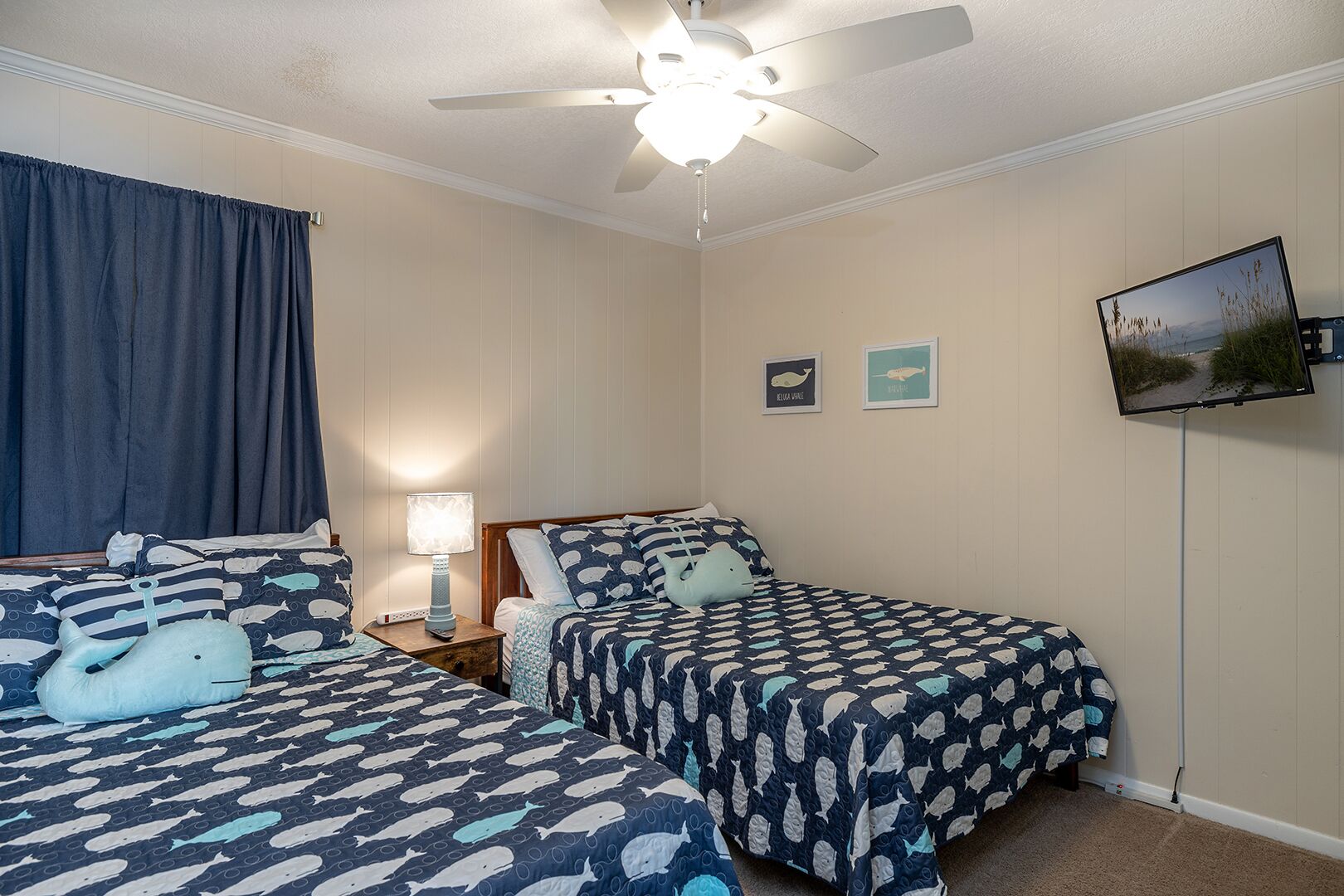 Une chambre avec deux lits, un ventilateur de plafond, une télévision et une lampe.