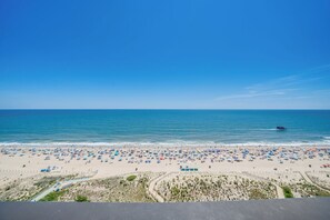 A beach with numerous umbrellas and people, a clear sky, and a calm sea.