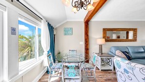 Una sala de estar acogedora con una mesa de comedor de cristal, sillas tapizadas en azul, un sofá azul y una viga de techo de madera.