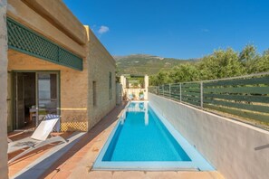A swimming pool with a view of mountains, a covered outdoor seating area, and a building with a stone facade. - Villa Mediterranea – Beachside Escape for Slow Living with Private Heated Pool (Livadia)