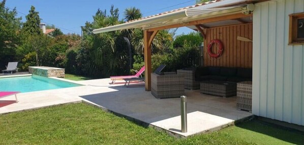 A backyard with a swimming pool, a covered patio area, and outdoor seating.