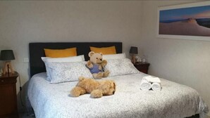 Un lit bien fait, avec un ours en peluche, une serviette enroulée et un oreiller.