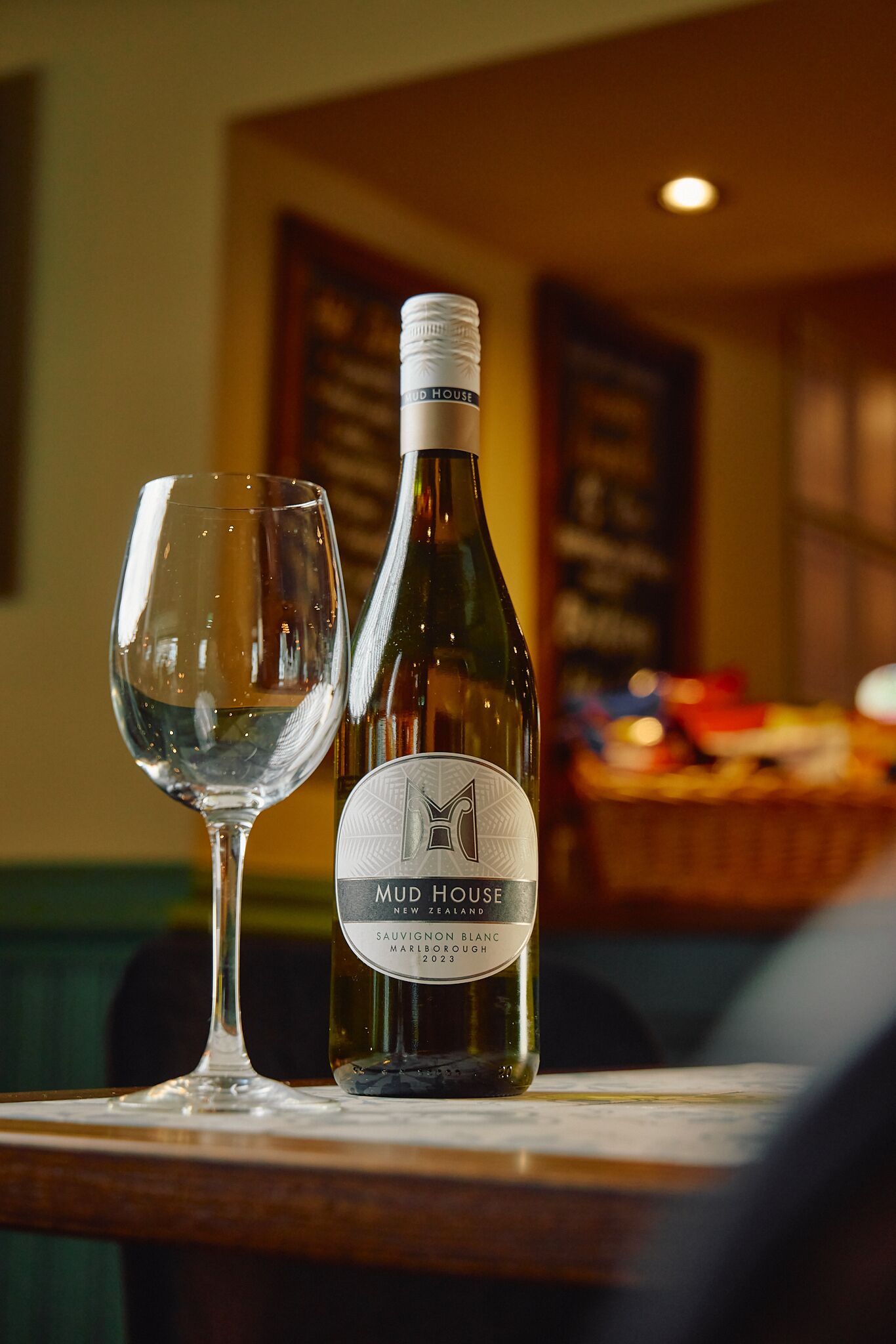 Eine Flasche Mud House Sauvignon Blanc und ein leeres Weinglas auf einem Tisch.