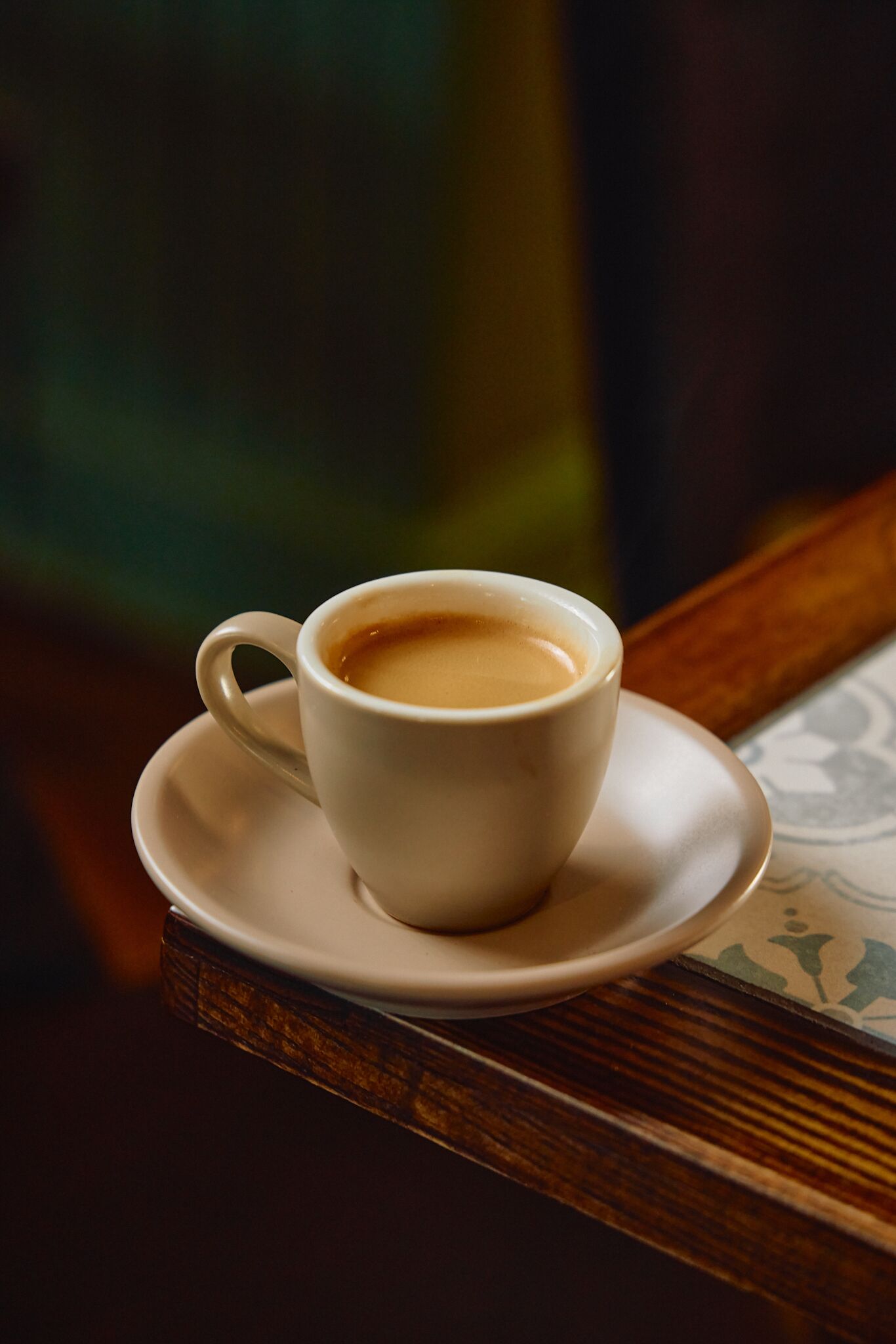 A white cup of coffee on a saucer on a wooden table.