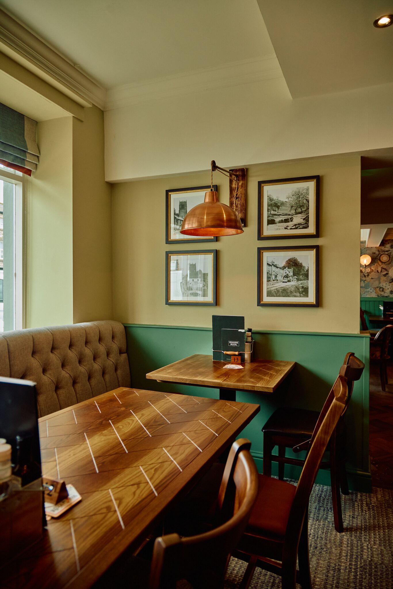 A restaurant with a wooden table and chairs, framed pictures on the wall, and a green accent wall.