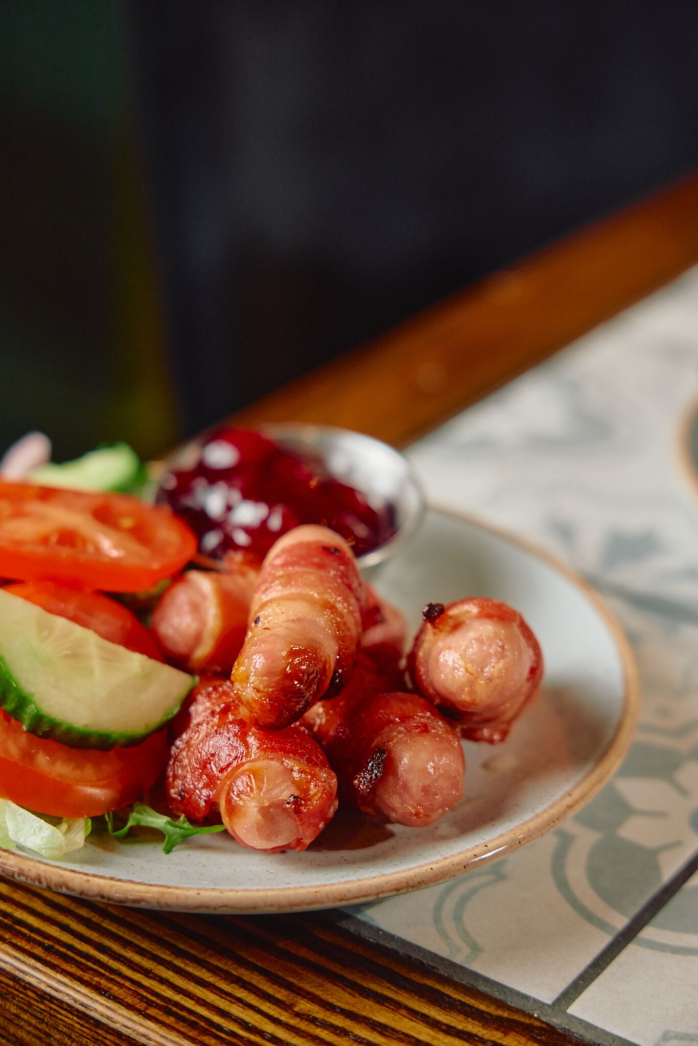 A plate of sausages with vegetables and a small bowl of sauce.