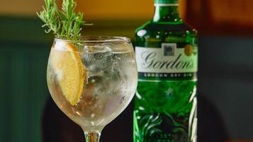 A cocktail glass with a lemon slice and a sprig of rosemary, next to a bottle of Gordon's London Dry Gin on a table with a patterned tablecloth.