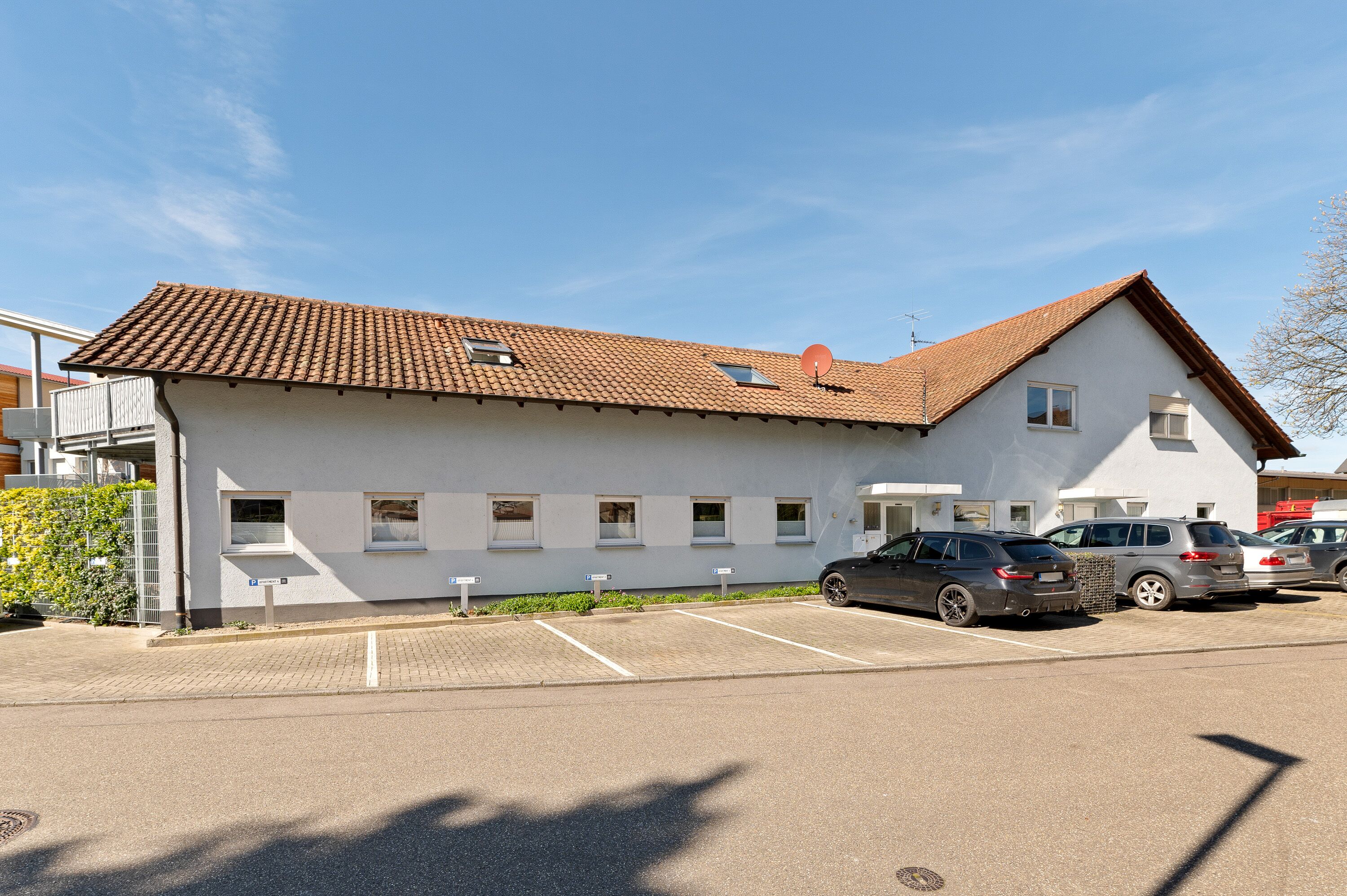 A building with a tiled roof, multiple windows, and a parking lot with several cars.