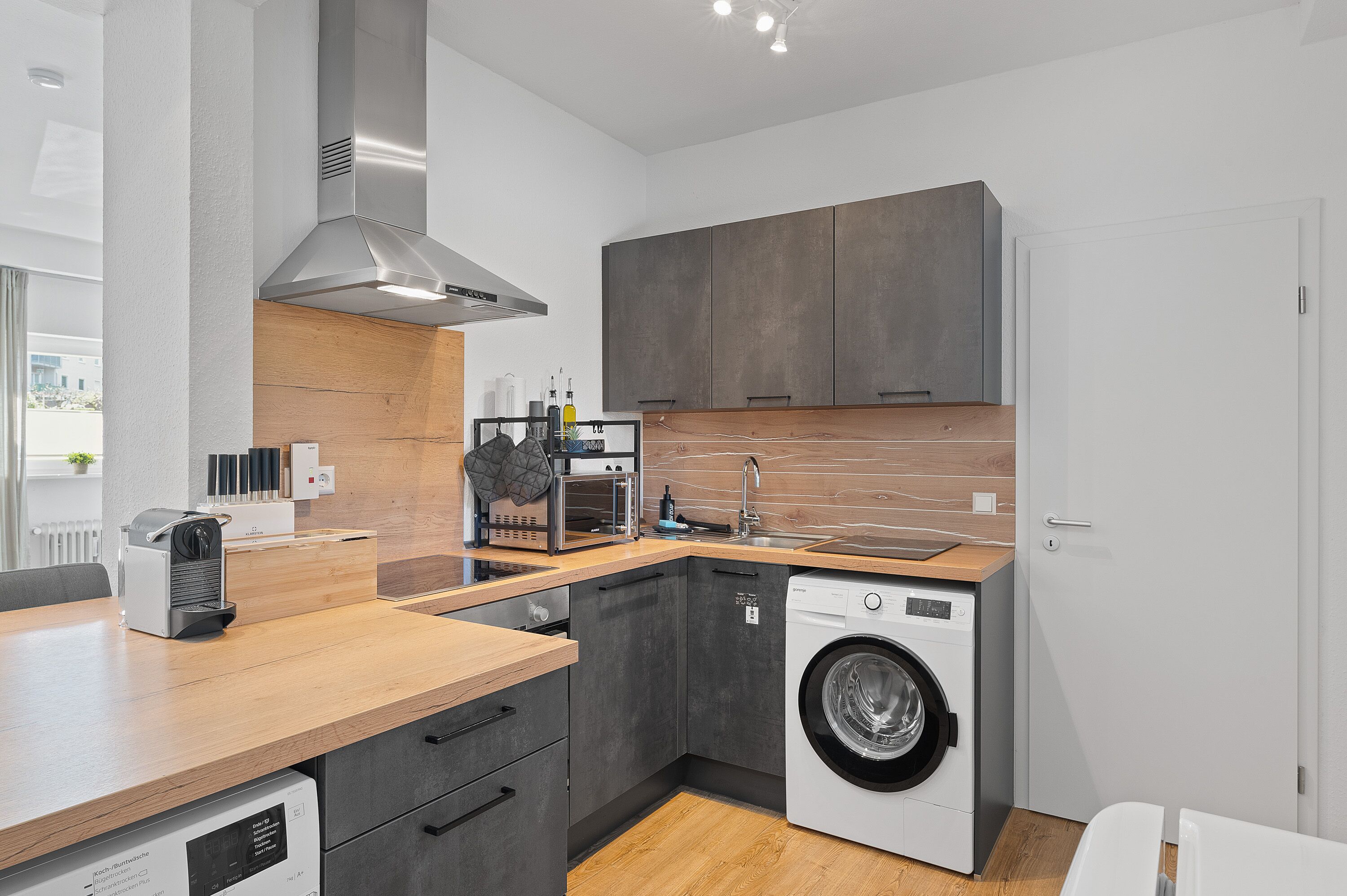 Una cocina moderna con lavadora integrada, encimera de madera y armarios grises.