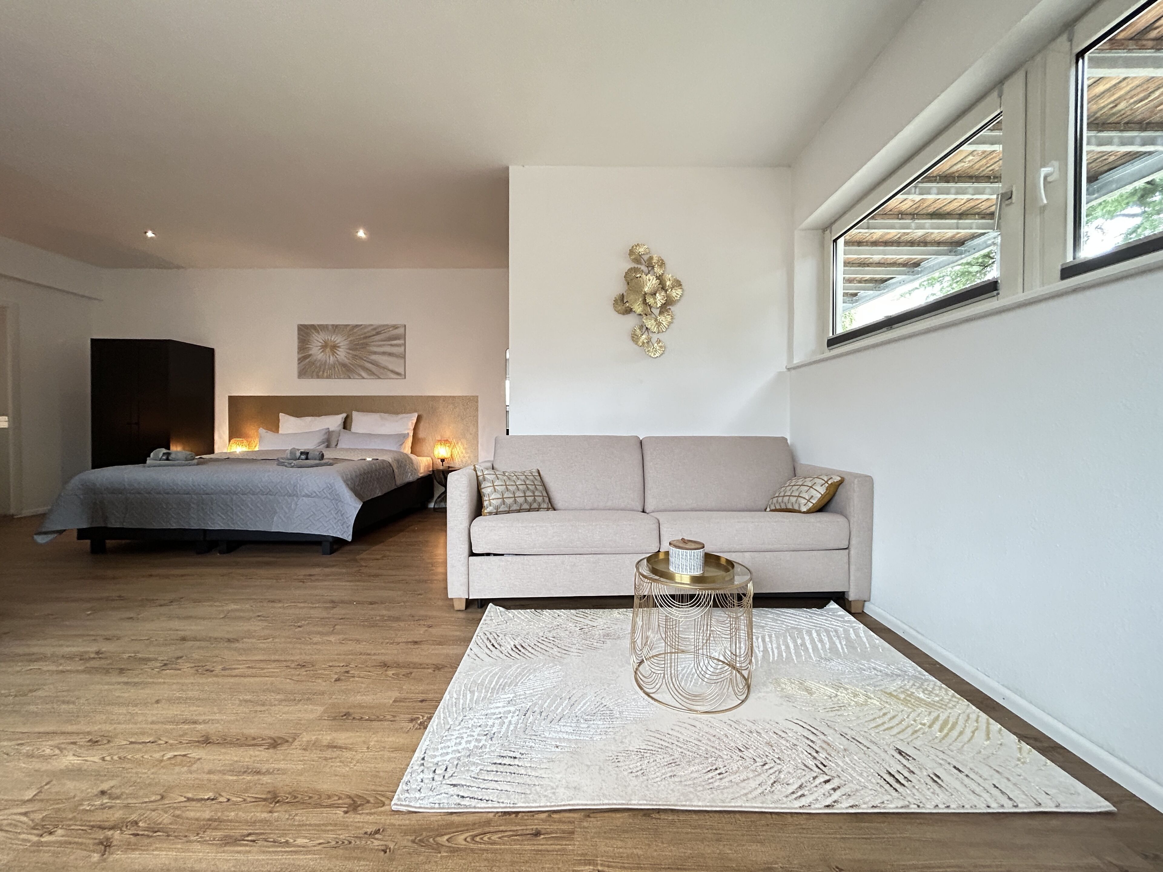 A modern bedroom with a large bed, a sofa, a decorative wall piece, and a window.