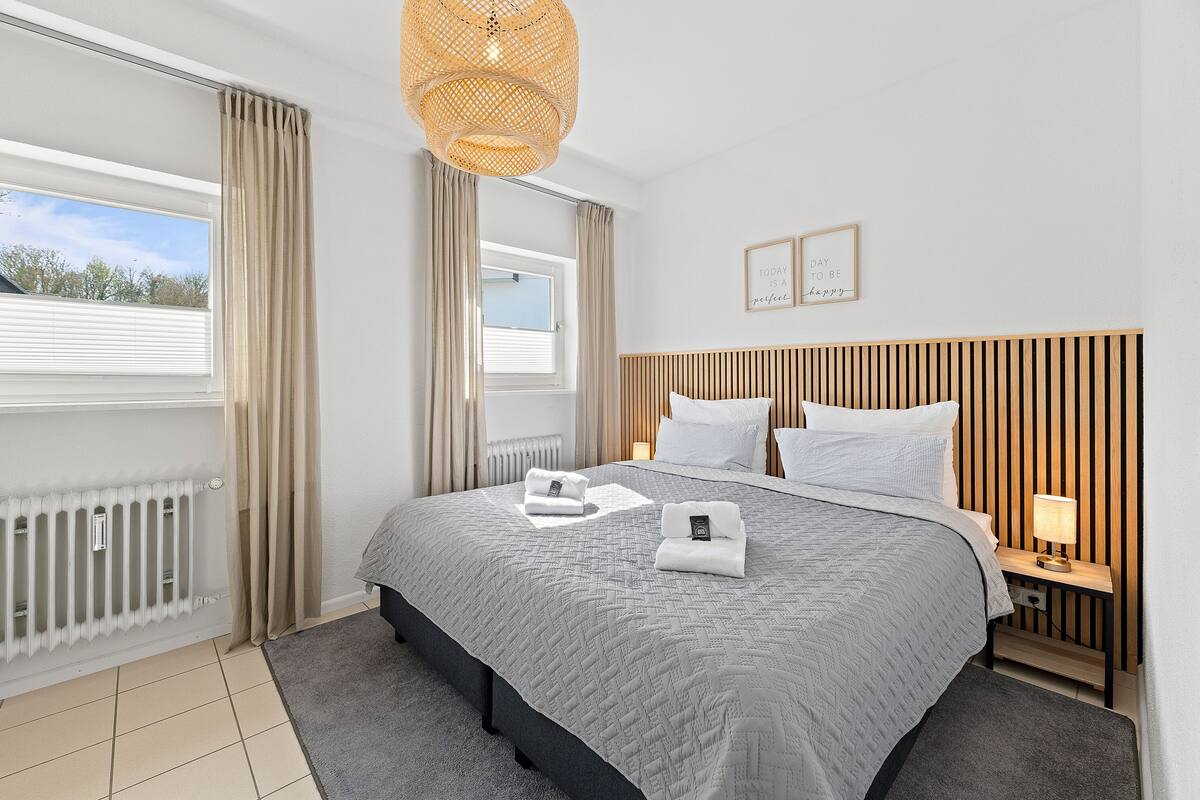 Habitación de hotel moderna con una cama grande, una mesita de noche con lámpara y vistas al exterior.