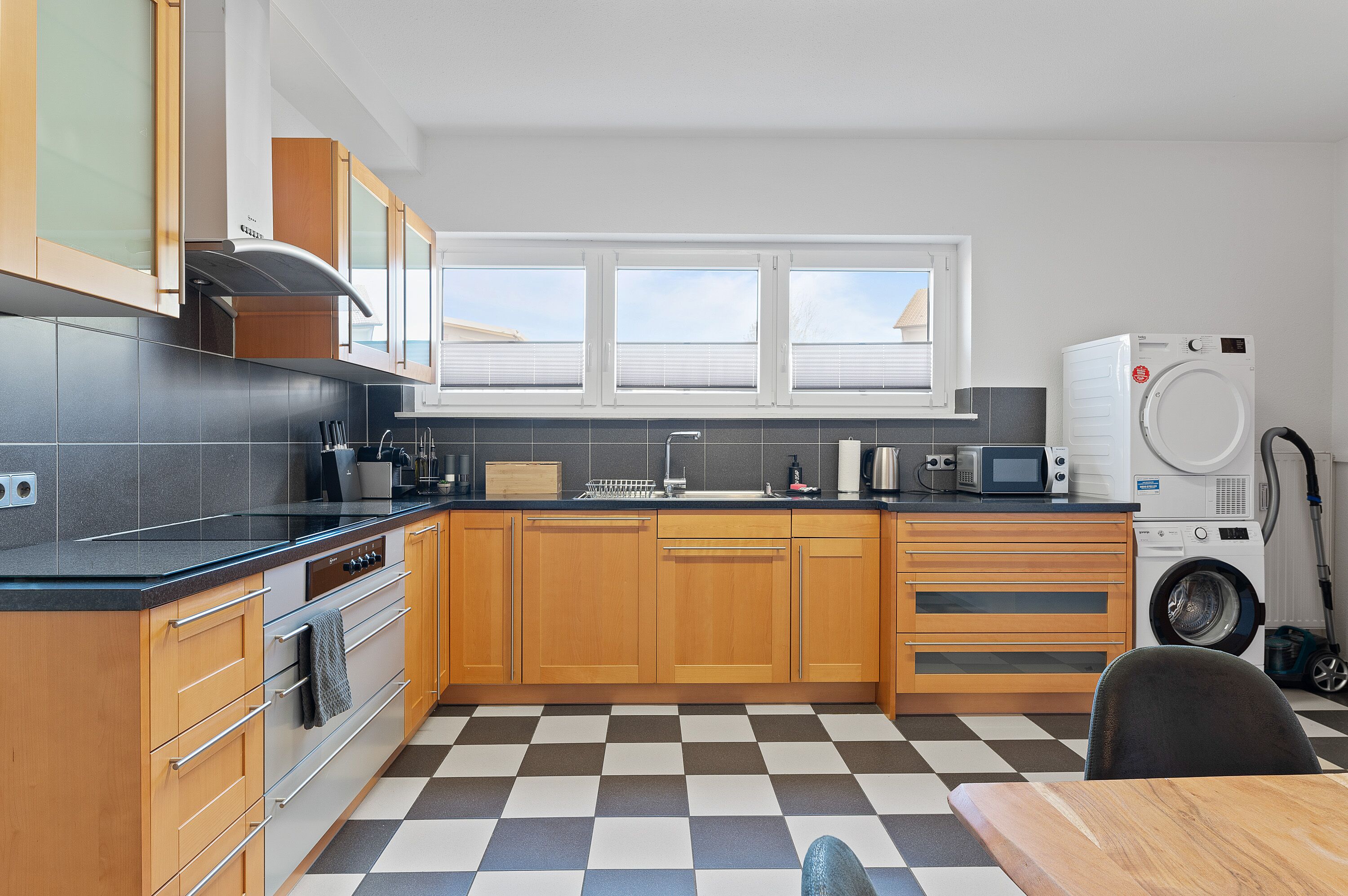 Eine moderne Küche mit Holzschränken, einer schwarzen Arbeitsplatte, einem eingebauten Backofen, einer Mikrowelle und einer Waschmaschine.