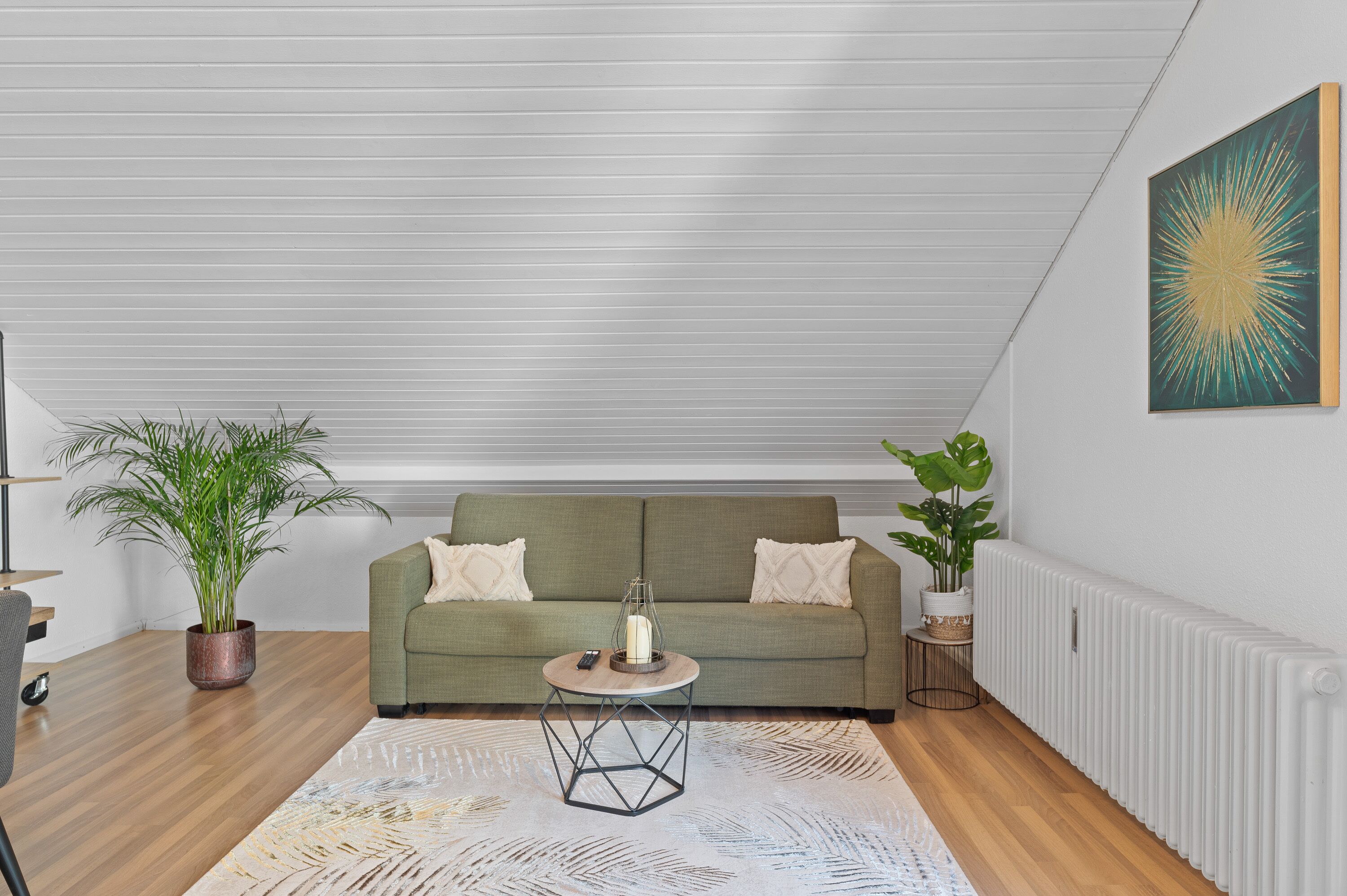 Ein modernes Wohnzimmer mit einem grünen Sofa, einem runden Couchtisch mit Kerze und zwei Zimmerpflanzen.