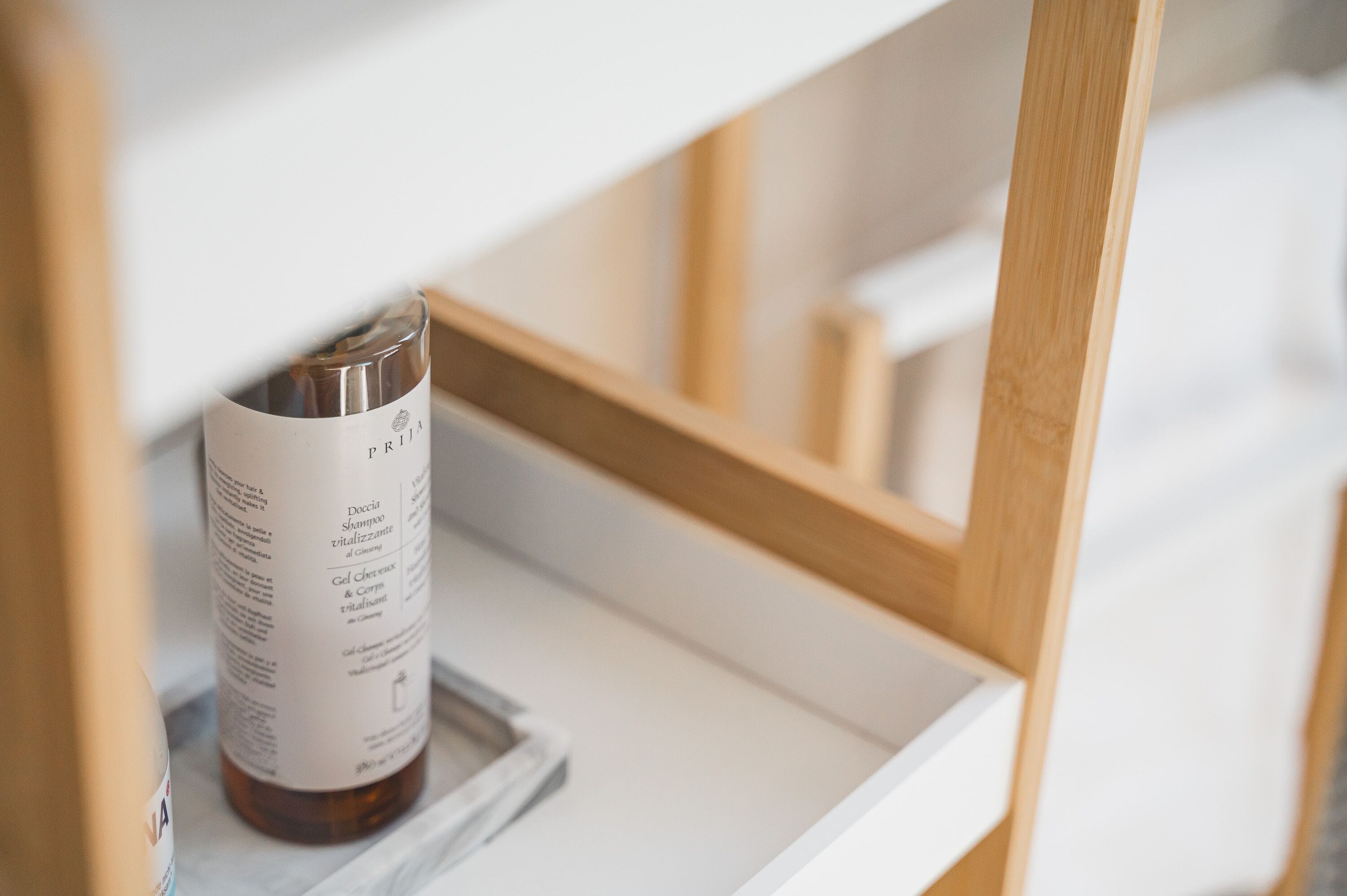 A bottle of shampoo on a white shelf in a room with wooden furniture.