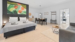 A modern bedroom with a large bed, a dining area with a table and chairs, and a sofa. - LUMIFLATS (Mahlberg)