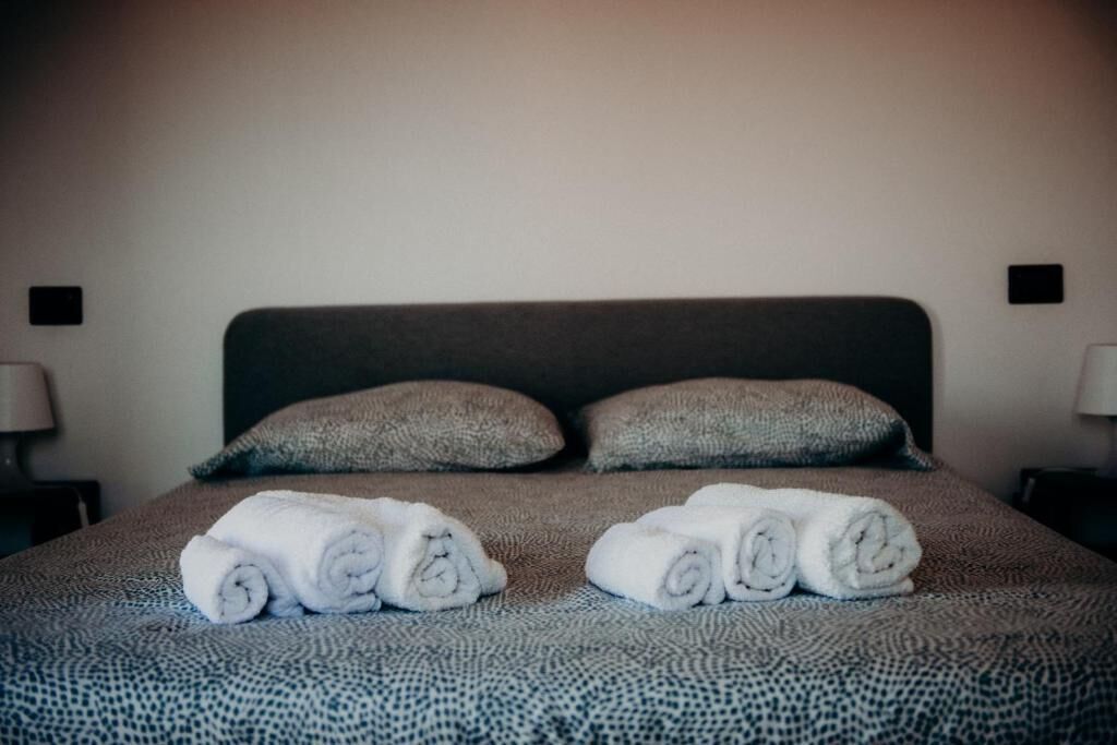 Ein ordentlich bezogenes Bett mit aufgerollten Handtüchern und zwei Kissen.