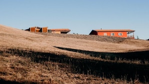 A building with a red facade and a sloped roof, situated on a grassy hill. - Azienda Agricola Saint Hubert (Cantalupo Ligure)