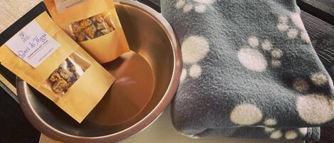 A bowl with two packets of Baci di Nocera, a grey blanket with paw prints, and a mat with a Saint Hubert's logo.
