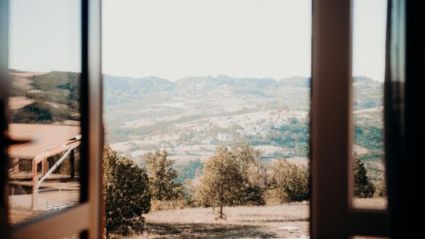 A view through a window of a rural landscape with rolling hills and a distant village. - Azienda Agricola Saint Hubert (Cantalupo Ligure)