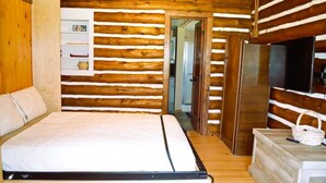 A log cabin room with a bed, a television, and a shelf with items. - Historic Cabin next to Custer State Park, Private (Custer)