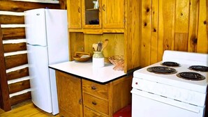 A compact kitchen with wooden cabinets, a white refrigerator, a stove, and a small countertop with kitchen utensils. - Historic Cabin next to Custer State Park, Private (Custer)