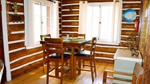 A wooden cabin interior with a dining table, chairs, and a small white table with decorative items. - Historic Cabin next to Custer State Park, Private (Custer)