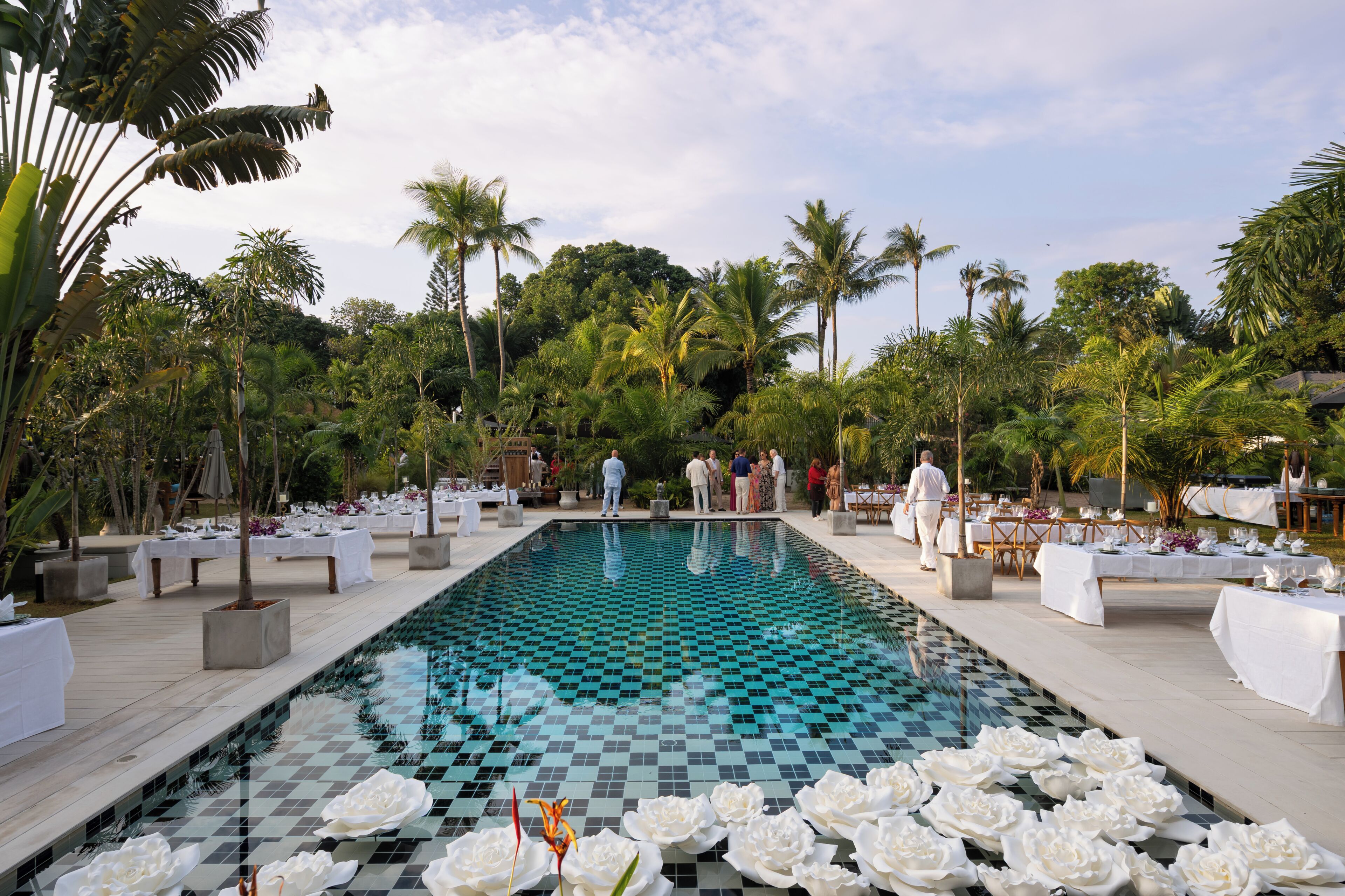 Ein Pool mit Schachbrettmuster, umgeben von Palmen und weißen Blumenarrangements.