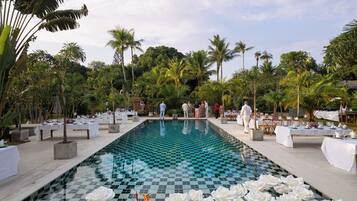 Ein Pool mit Schachbrettmuster, umgeben von Palmen und weißen Blumenarrangements.