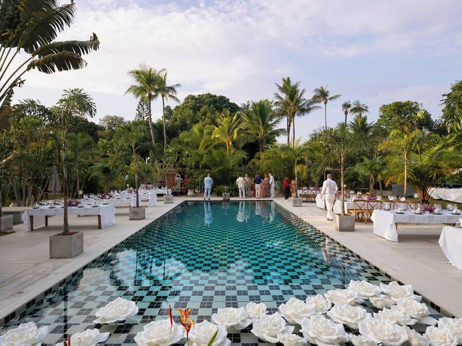 Ein Pool mit Schachbrettmuster, umgeben von Palmen und weißen Blumenarrangements.