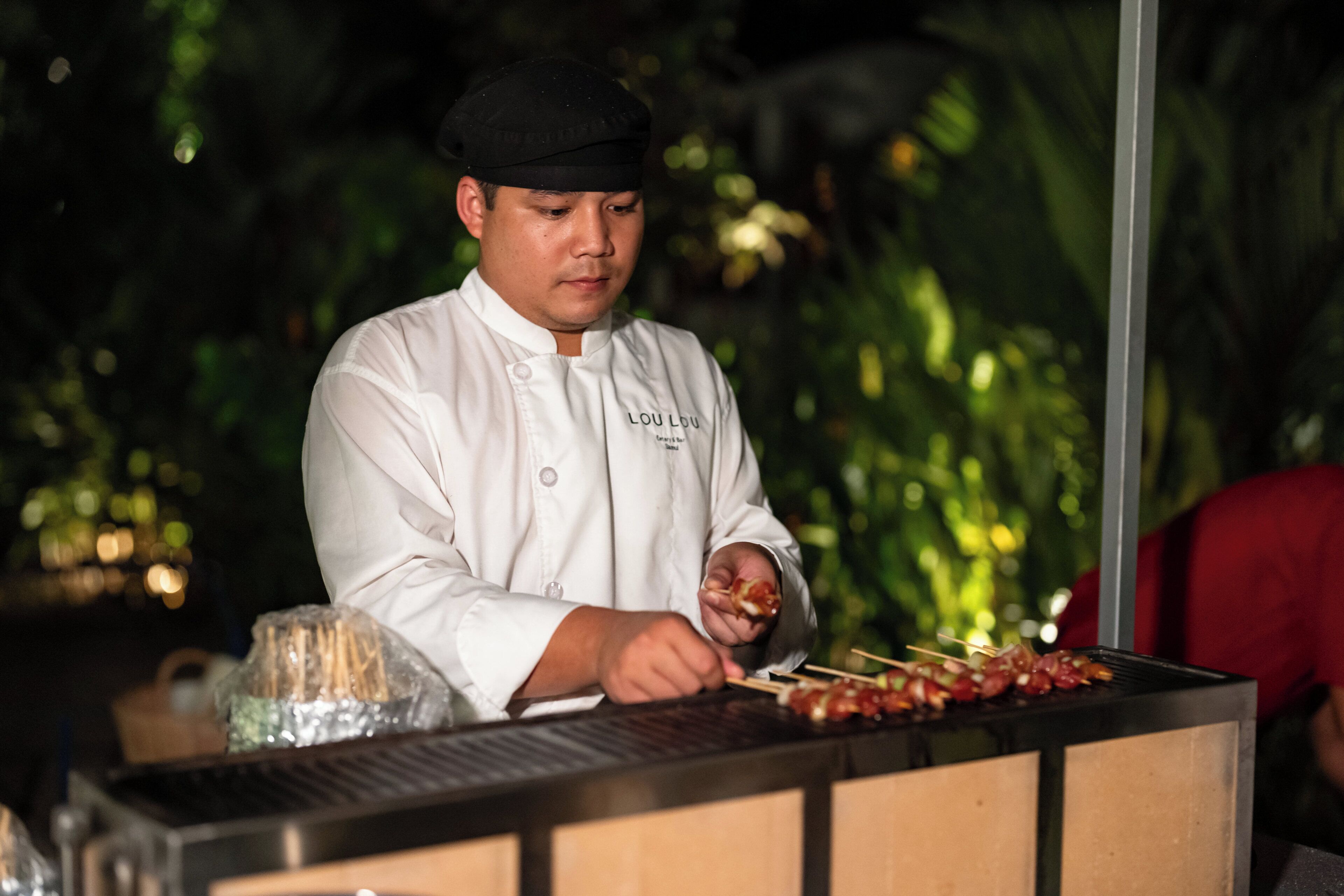 A chef in a white uniform preparing food at a grill station.