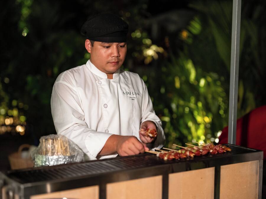 A chef in a white uniform preparing food at a grill station.
