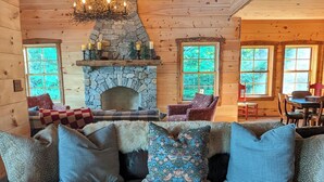 A cozy cabin interior with a stone fireplace, wooden walls, and a leather sofa with patterned cushions.