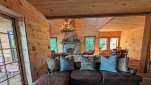 A cozy cabin interior with a stone fireplace, wooden walls, and a leather sofa with patterned cushions.