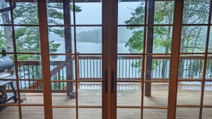 A room with large sliding glass doors leading to a wooden deck overlooking a lake.