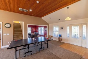 A room with a ping pong table, a staircase, a dining area, and a door leading outside.