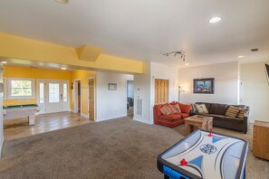 A spacious living room with a pool table, a red sofa, and a brown couch.