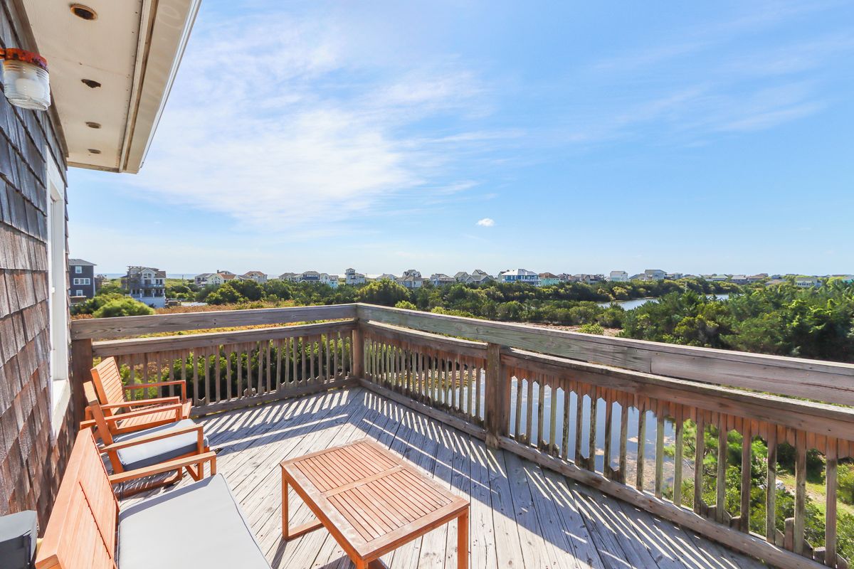 A wooden deck with a table and chairs, overlooking a body of water and greenery.
