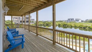 A wooden deck with blue chairs overlooking a calm body of water and buildings in the background.