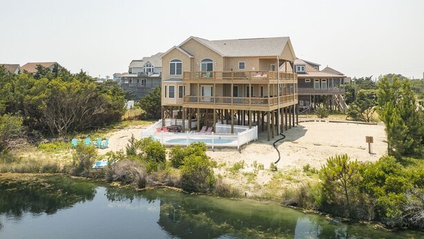 A multi-story beachfront house with a pool, deck, and pier.