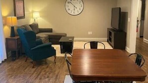 Una sala de estar con una mesa de comedor de madera, sillones azules, un sofá, un reloj y un televisor.