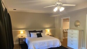 Un dormitorio con cama, dos lámparas de noche, ventilador de techo, cómoda y vestidor.