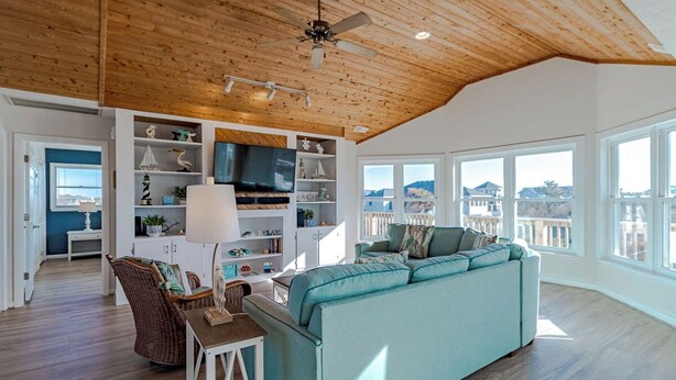 Een ruime woonkamer met een hoge plafond, inbouwkasten, een smaragdgroene bank en een eethoek.
