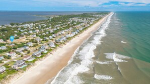 Luchtbeeld van een kustgebied met woningen langs het strand, een heldere lucht en een rustige zee.