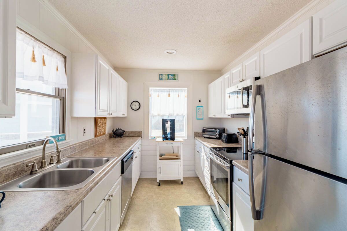 A kitchen with white cabinets, stainless steel appliances, and a window with sheer curtains.