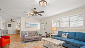 A spacious living room with a blue sofa, a gray sofa, and a red chair. There are ceiling fans, a coffee table, and a patterned rug. - Throw Em Back Inn, Dog Friendly! (Port Aransas)